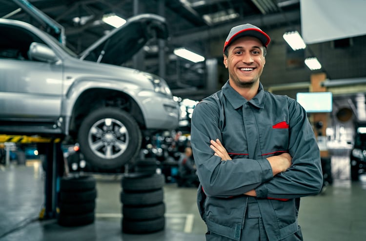 Auto repair shop technician smiling in front of a lifted vehicle.