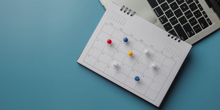 Paper calendar with appointments marked laying over a Mac computer