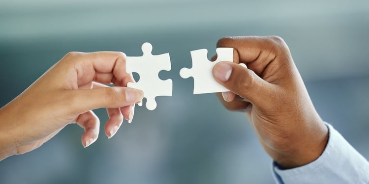 Two business people holding two puzzle pieces that fit together.