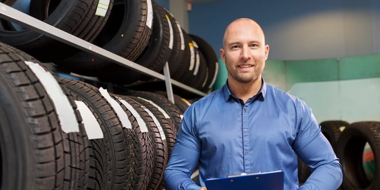 A tire shop owner standing in front of a row of tires